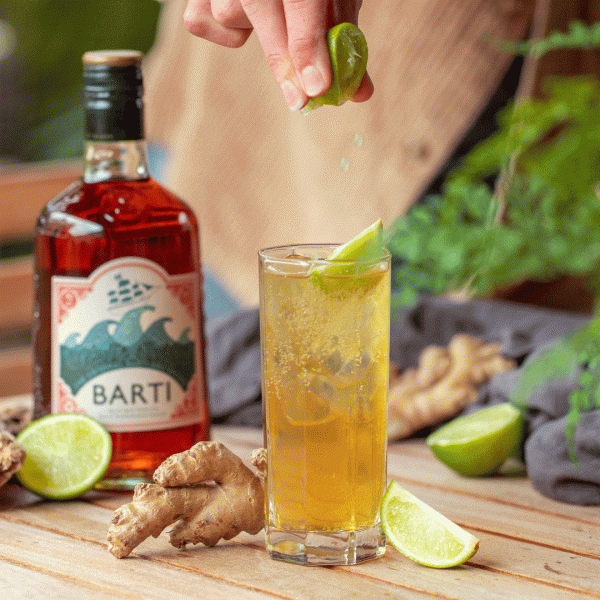 Spiced rum with ginger beer in a tall glass with ginger and lime garnish
